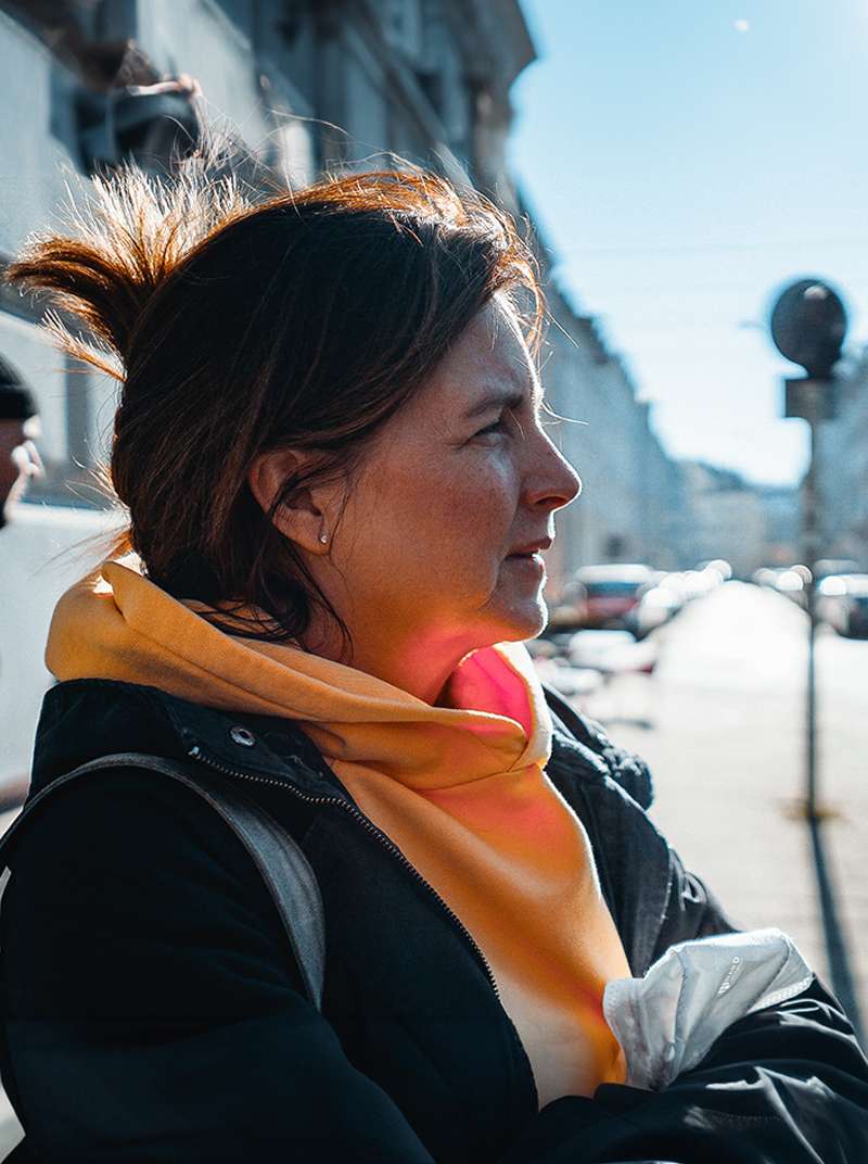 Siggi steht in der Sonne und ist im Profil zu sehen. Sie trägt einen orangenen Pulli und hat die Augen ein bisschen zusammengekniffen.